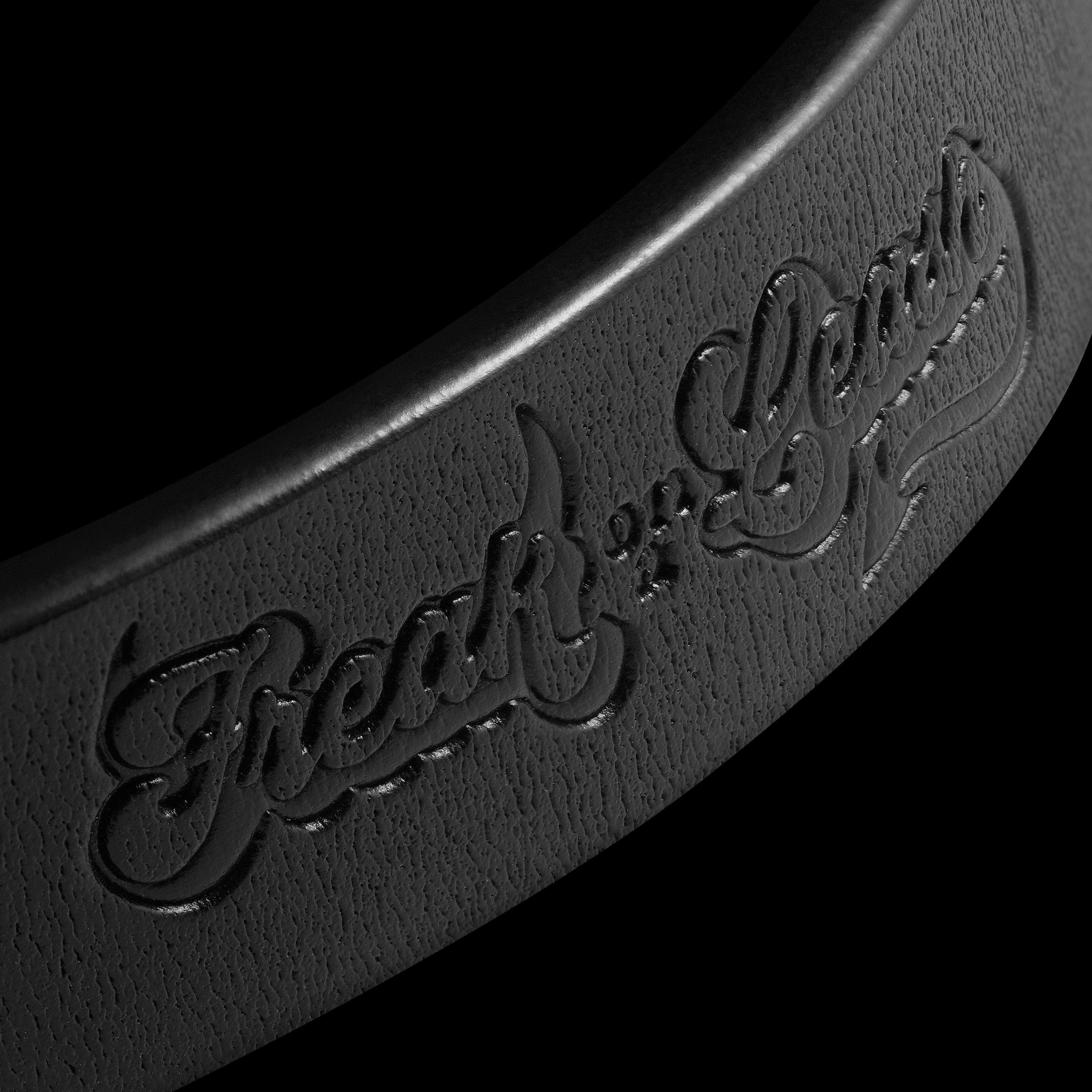 Close-up of Freak On A Leash black leather dog collar showing debossed logo and natural grain texture
